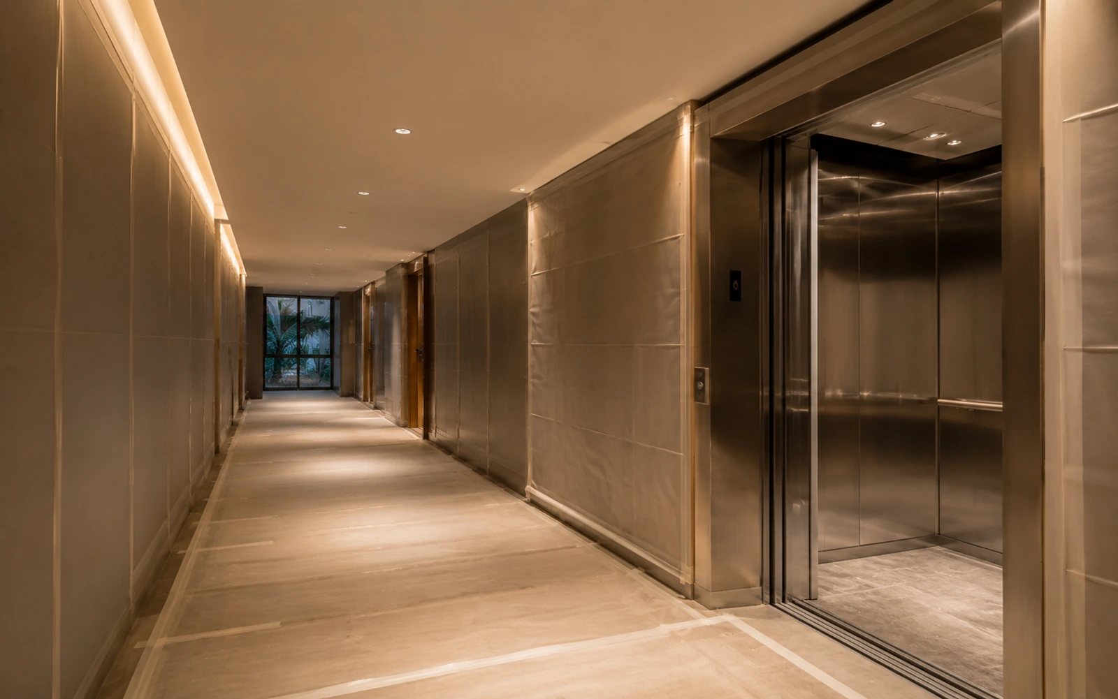Service corridor of a luxury Miami residential tower prepared for construction access, with protective wall panels, covered flooring and an open stainless steel service elevator