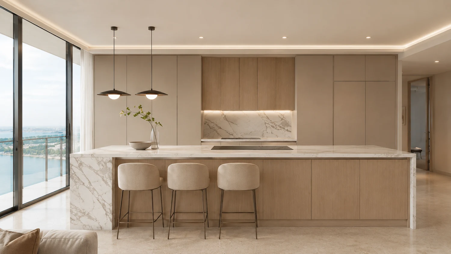 Contemporary kitchen in a Miami condominium tower with a book matched marble island and waterfall edge, pale oak and warm greige handleless cabinetry, two bronze pendants, cream boucle stools, and a clean ceiling with no extraction hood or ductwork