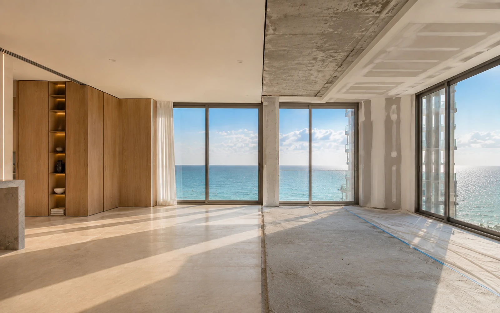 Luxury oceanfront condominium interior in Miami where finished stone flooring and pale oak millwork meet exposed concrete structure, showing the boundary between the unit and the building