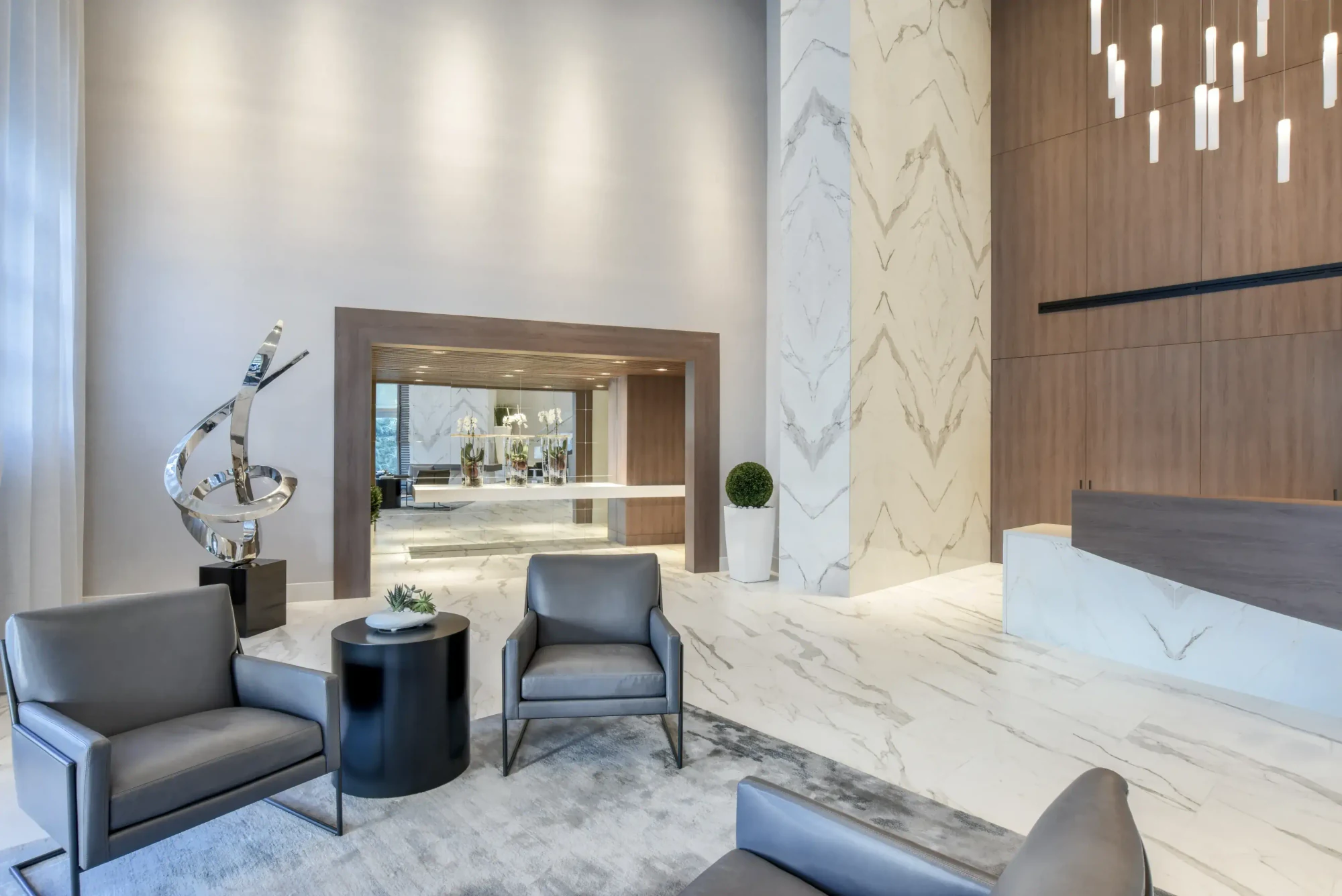 Lobby seating area at the Diplomat Residences in Hollywood, Florida, with book-matched marble walls, grey leather armchairs and a sculptural artwork