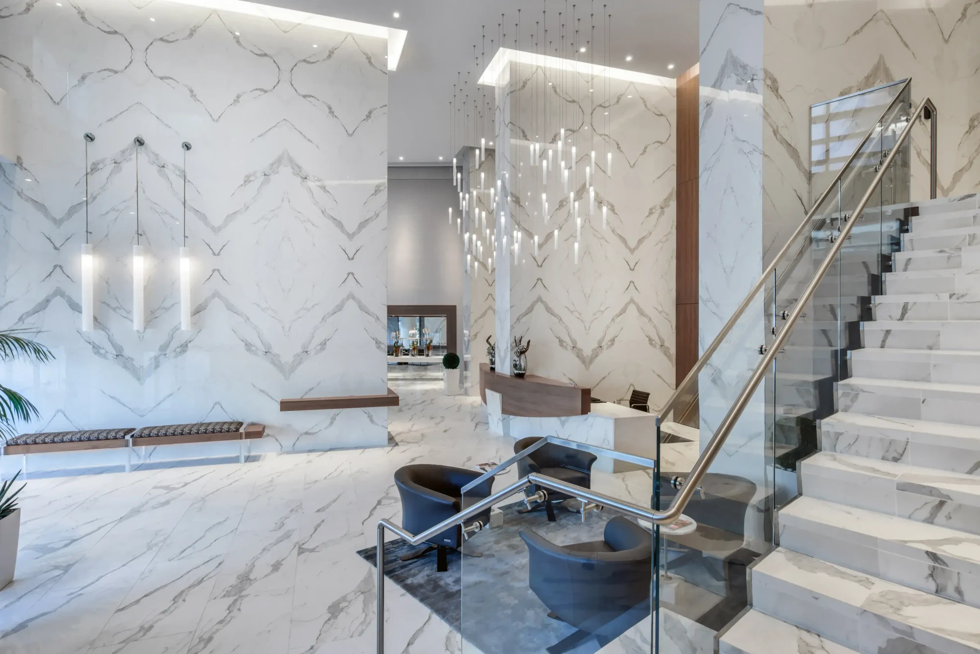 Lobby at the Diplomat Residences in Hollywood, Florida, with a chevron book-matched marble wall, glass staircase and hanging crystal fixture