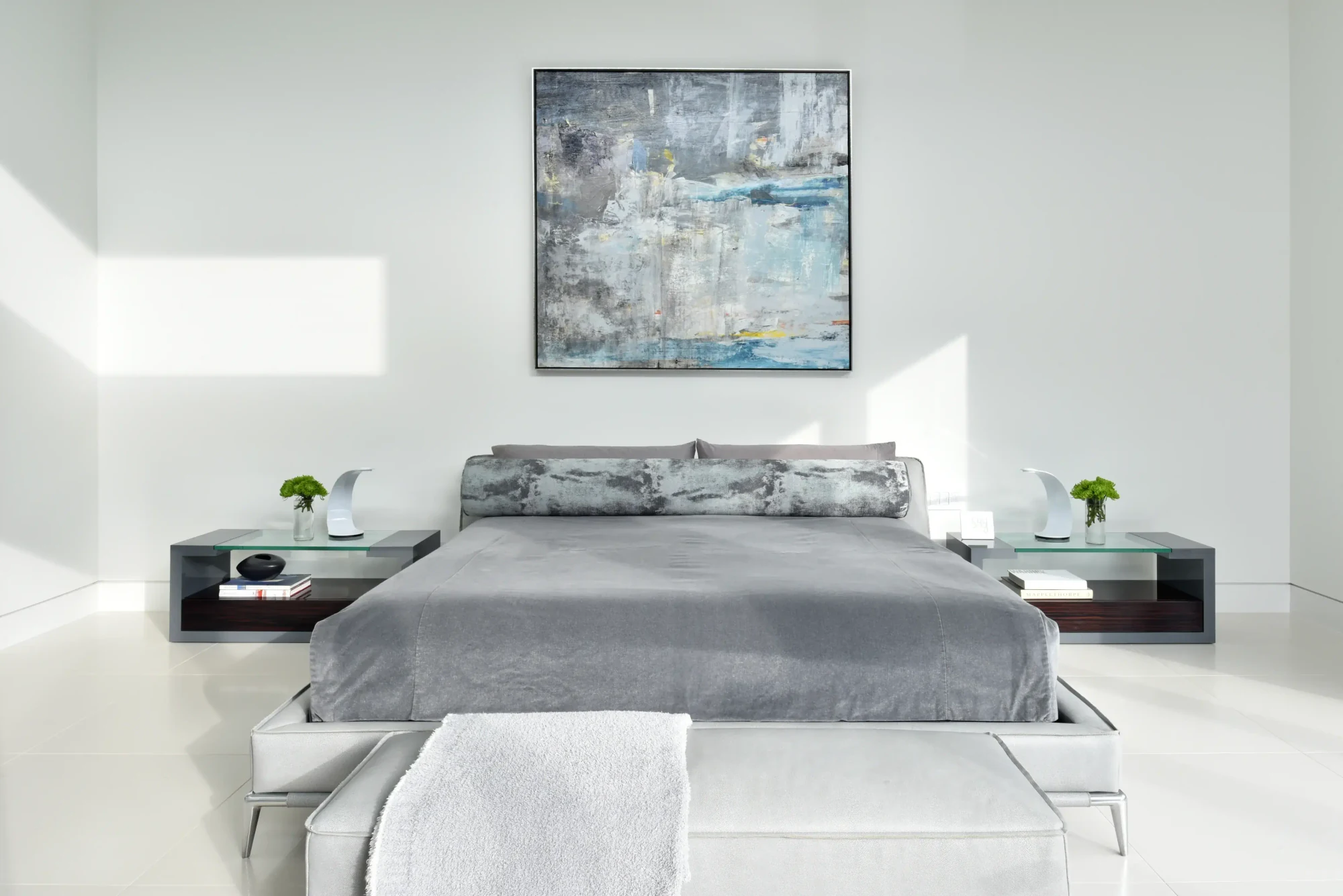 Primary bedroom at the Richfield Residence in Davie, Florida, with an abstract canvas, glass nightstands and layered grey bedding