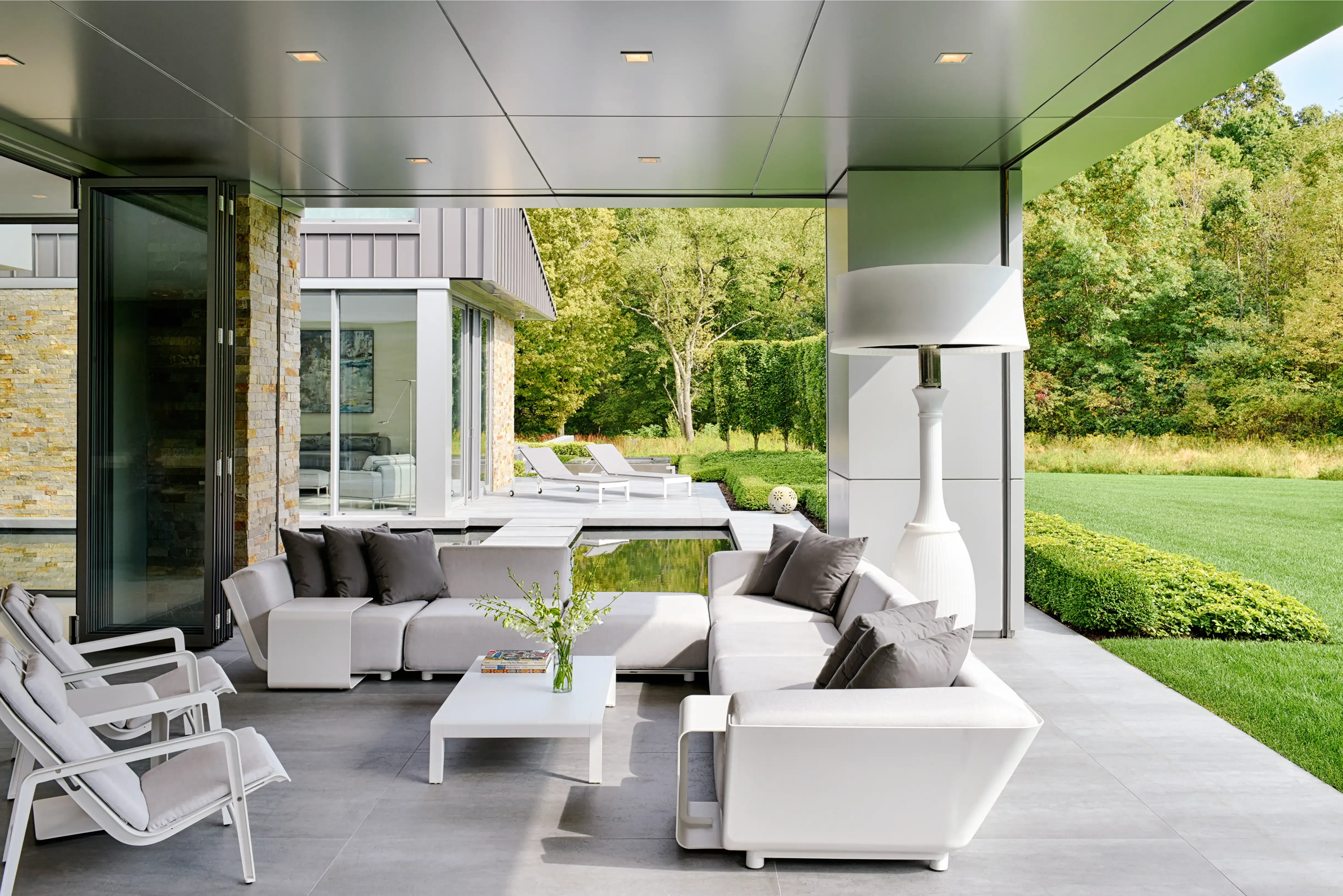 Covered outdoor living terrace at the Richfield Residence in Davie, Florida, with white lounge seating and lawn beyond
